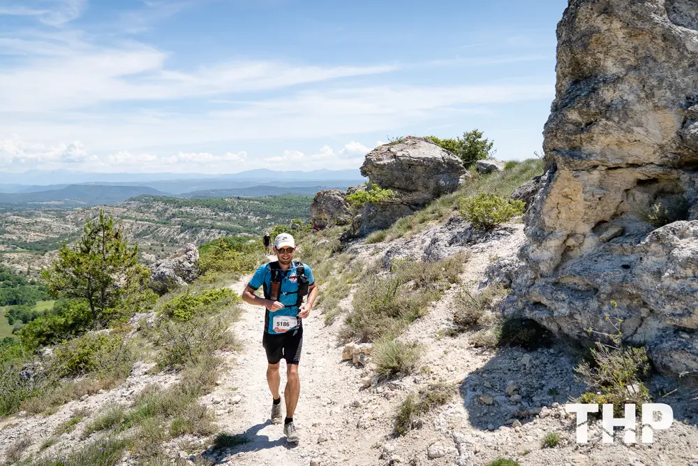 Un coureur déterminé affronte les sentiers escarpés de la Haute Provence lors du meilleur trail France, THP Summer. Son numéro 5186 brille sous le soleil, tandis qu'il profite d'une vue imprenable sur des paysages sauvages et lumineux, alliant aventure, défi sportif et émotion pure.